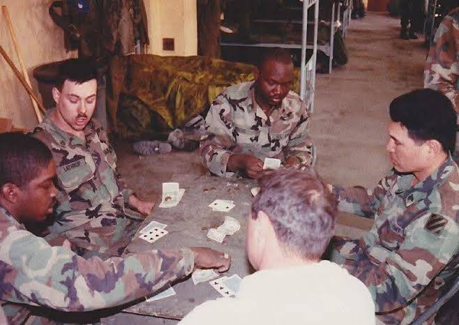 Soldiers and a fellow player gathered around a table playing cards.